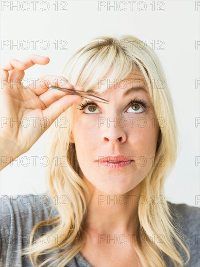 Studio portrait of blonde woman with tweezers