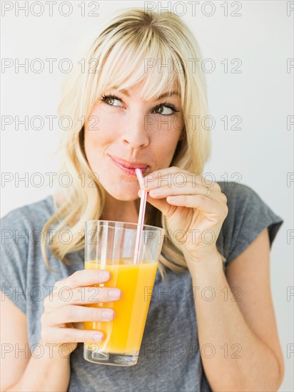 Studio portrait of blonde woman drinking orange juice