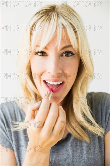 Woman applying lipstick, studio shot