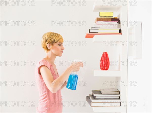 Young woman cleaning bookshelf