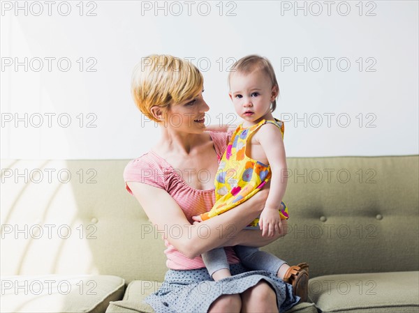 Mother with daughter (12-17 months) sitting on sofa