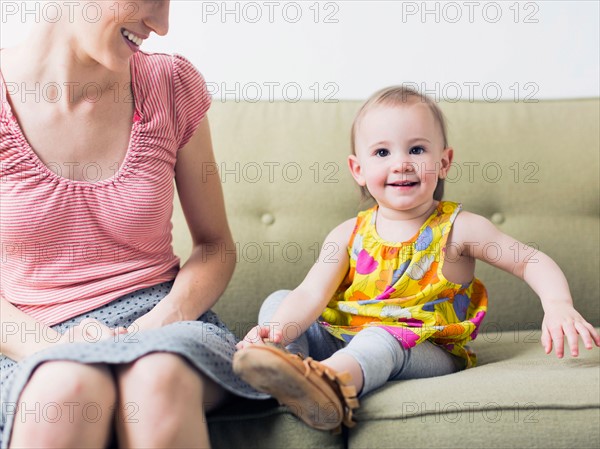 Mother with daughter (12-17 months) sitting on sofa