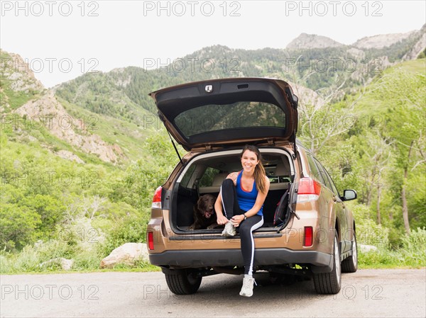 Woman wearing sportswear sitting at car trunk with dog