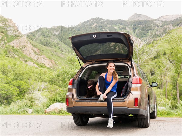 Woman wearing sportswear sitting at car trunk with dog