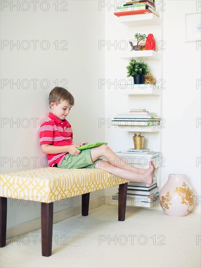 Boy (6-7) sitting on bench using digital tablet