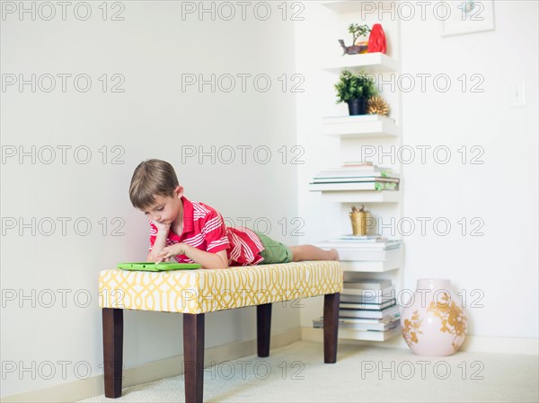 Boy (6-7) lying on bench using digital tablet