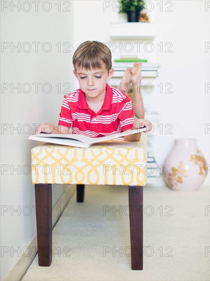 Boy (6-7) lying on bench reading book