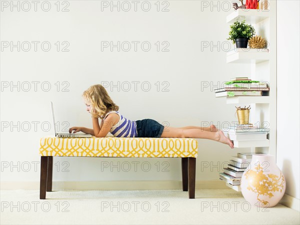 Girl (4-5) lying on bench using laptop