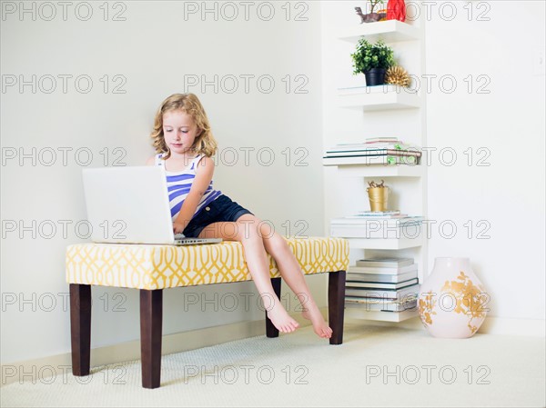 Girl (4-5) sitting on bench using laptop