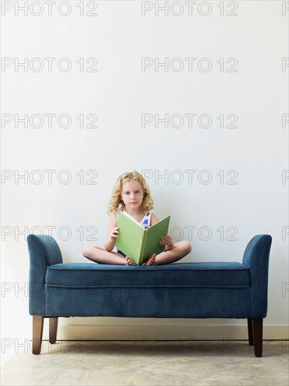 Girl (4-5) sitting on bench and reading book
