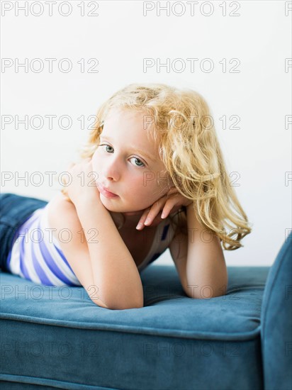 Portrait of girl (4-5) lying on bench indoors