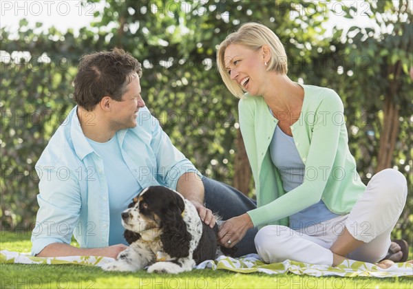 Couple with dog relaxing on grass.