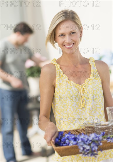 Woman carrying tray with crockery and flowers.