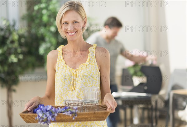 Woman carrying tray with crockery and flowers.