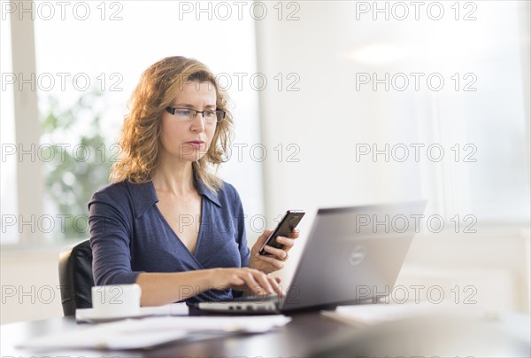 Businesswoman using laptop and phone.