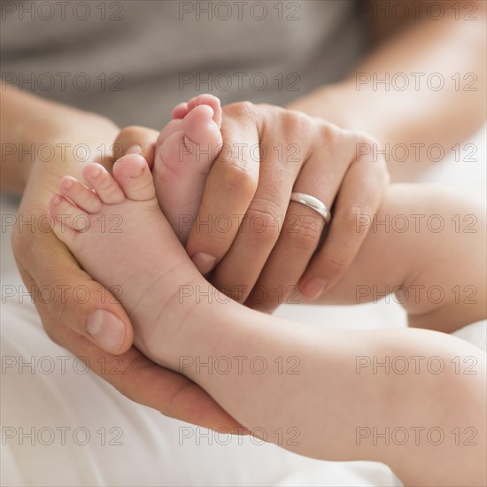 Mother holding baby boy's (2-5 months) feet.