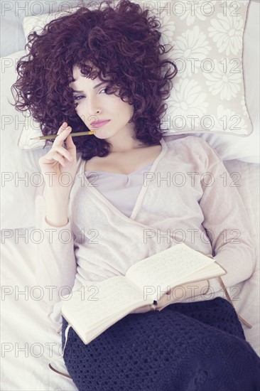 Portrait of beautiful brunette woman lying on bed with diary.