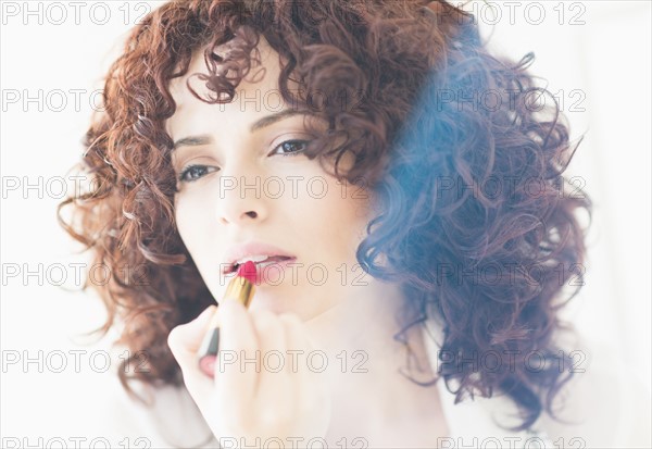 Studio shot of beautiful woman applying lipstick.