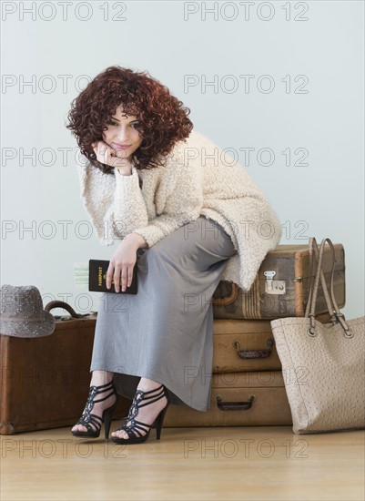 Woman sitting on stack of vintage suitcases.