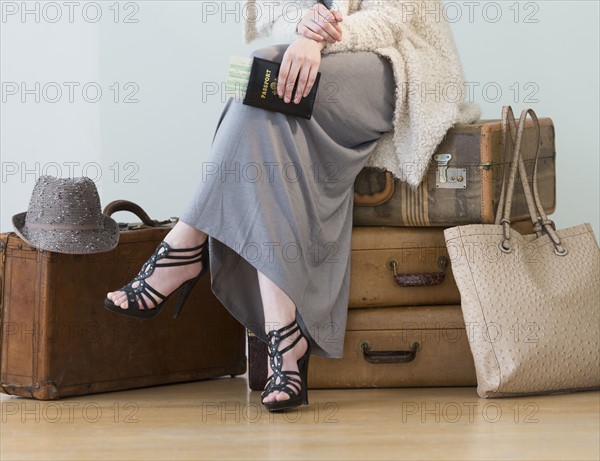 Woman sitting on stack of vintage suitcases.