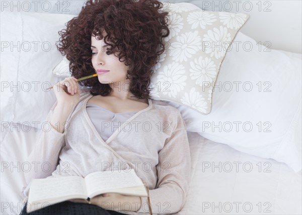 Beautiful woman lying in bed holding diary.