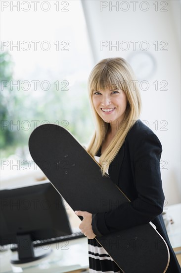 Businesswoman holding skateboard in office.
Photo : Jamie Grill