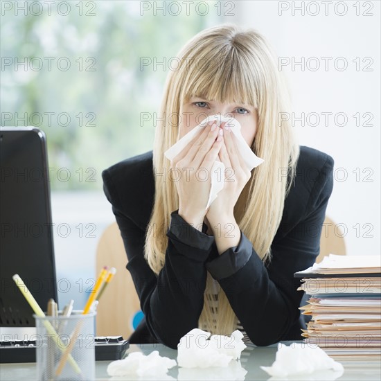 Businesswoman blowing nose in office.
Photo : Jamie Grill