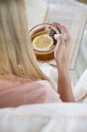 Woman holding tea cup and reading book.
Photo : Jamie Grill