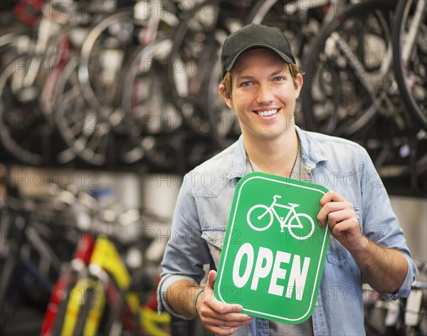 Portrait of man in bike shop holding open sign.
Photo : Daniel Grill