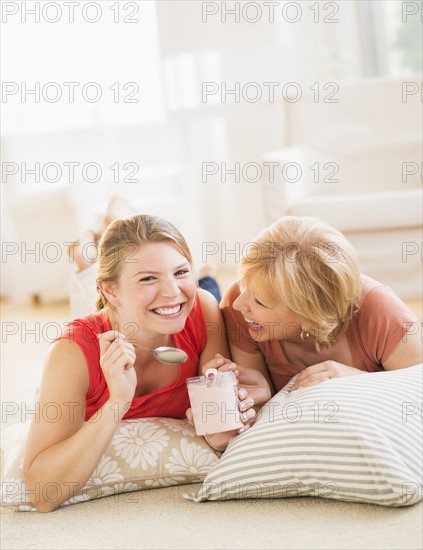 Mother and adult daughter relaxing at home, eating ice cream.
Photo : Daniel Grill