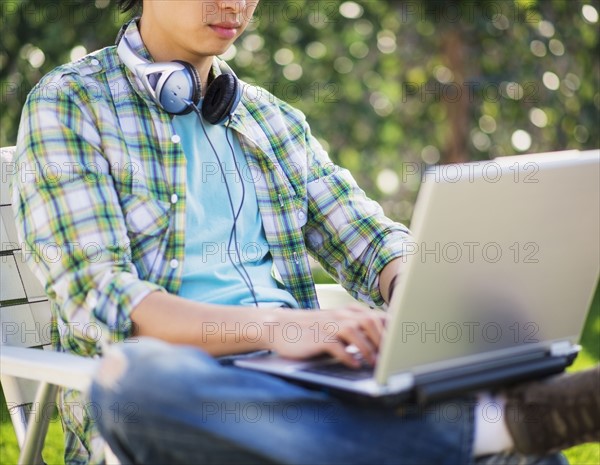 Teenage boy (16-17) using laptop in park, mid-section.
Photo : Daniel Grill