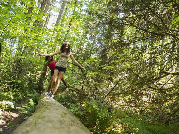 Two young women walking on log in forest. USA, Oregon, Portland.