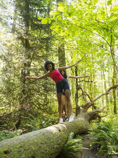 Two young women walking on log in forest. USA, Oregon, Portland.