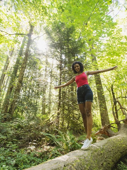 Young woman walking on log in forest. USA, Oregon, Portland.