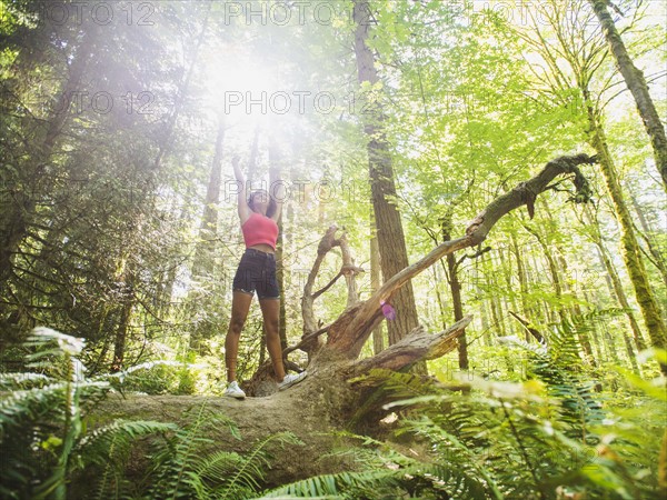 Young woman standing on log in forest. USA, Oregon, Portland.