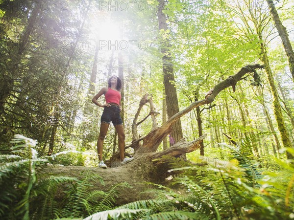 Young woman standing on log in forest. USA, Oregon, Portland.