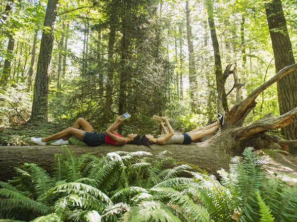 Young women reading book on log in forest. USA, Oregon, Portland.