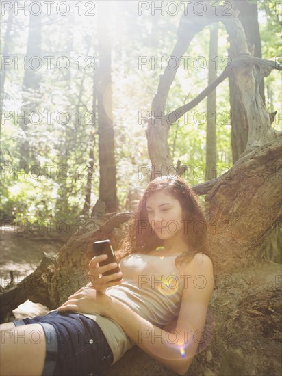 Young woman sitting on log and text messaging. USA, Oregon, Portland.