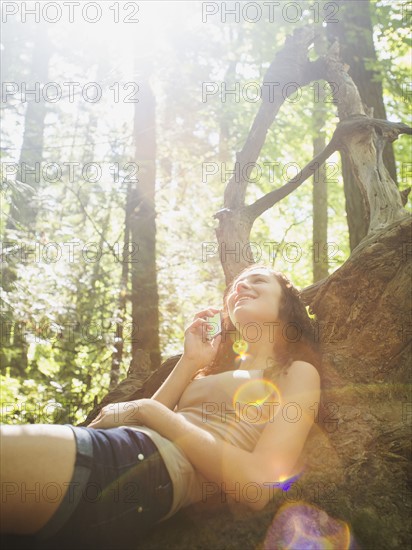 Young woman sitting on log and using cell phone. USA, Oregon, Portland.