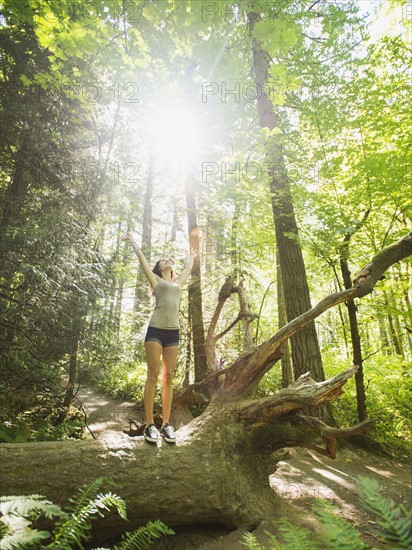 Young woman standing on log with arms raised. USA, Oregon, Portland.