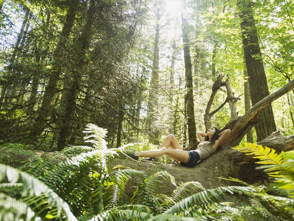 Young woman lying down on log. USA, Oregon, Portland.