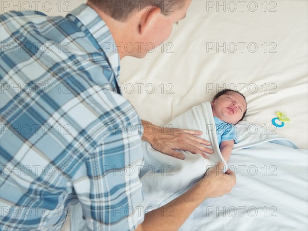 Father wrapping newborn son (0-11 months) in blanket.