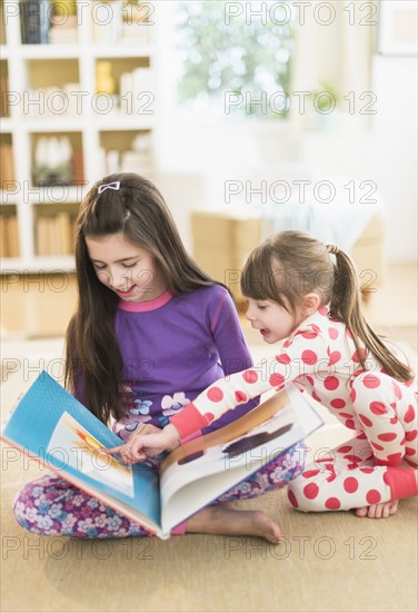 Two sisters (4-5, 8-9) reading picture book.