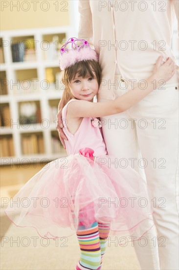 Girl (4-5) wearing tutu holding onto mother.