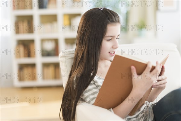 Girl (8-9) reading book in armchair.