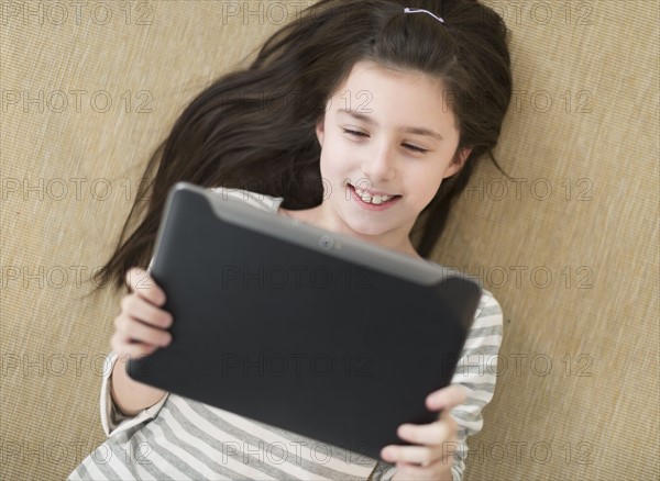 Girl (8-9) lying on floor using tablet pc.