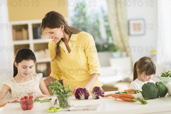 Mother and daughters (4-5, 8-9) cooking in kitchen.