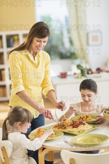 Mother and daughters (4-5, 8-9) eating pasta.