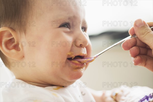 Close-up of baby girl (12-17 months) being spoon fed.