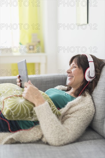 Woman relaxing on sofa, listening to music on tablet pc.